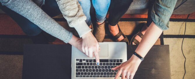 Three people point at a silver laptop screen.