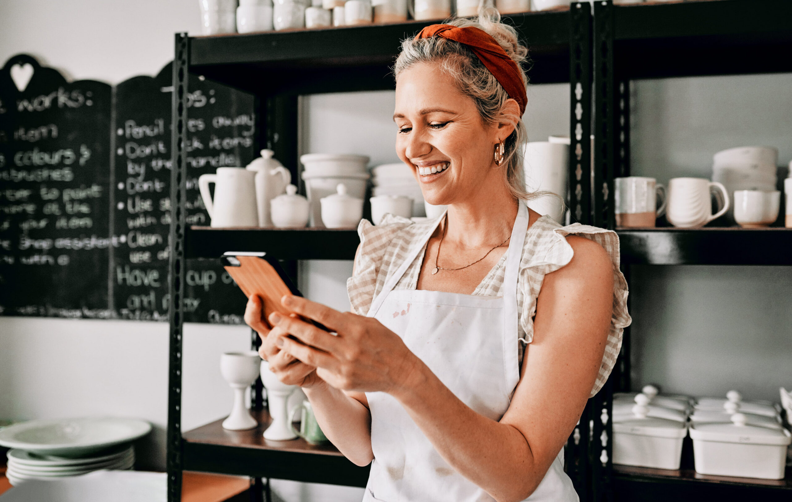 Smiling small business owner in a retail shop using a smartphone to manage her online business presence, highlighting the importance of staying active and visible to local customers.