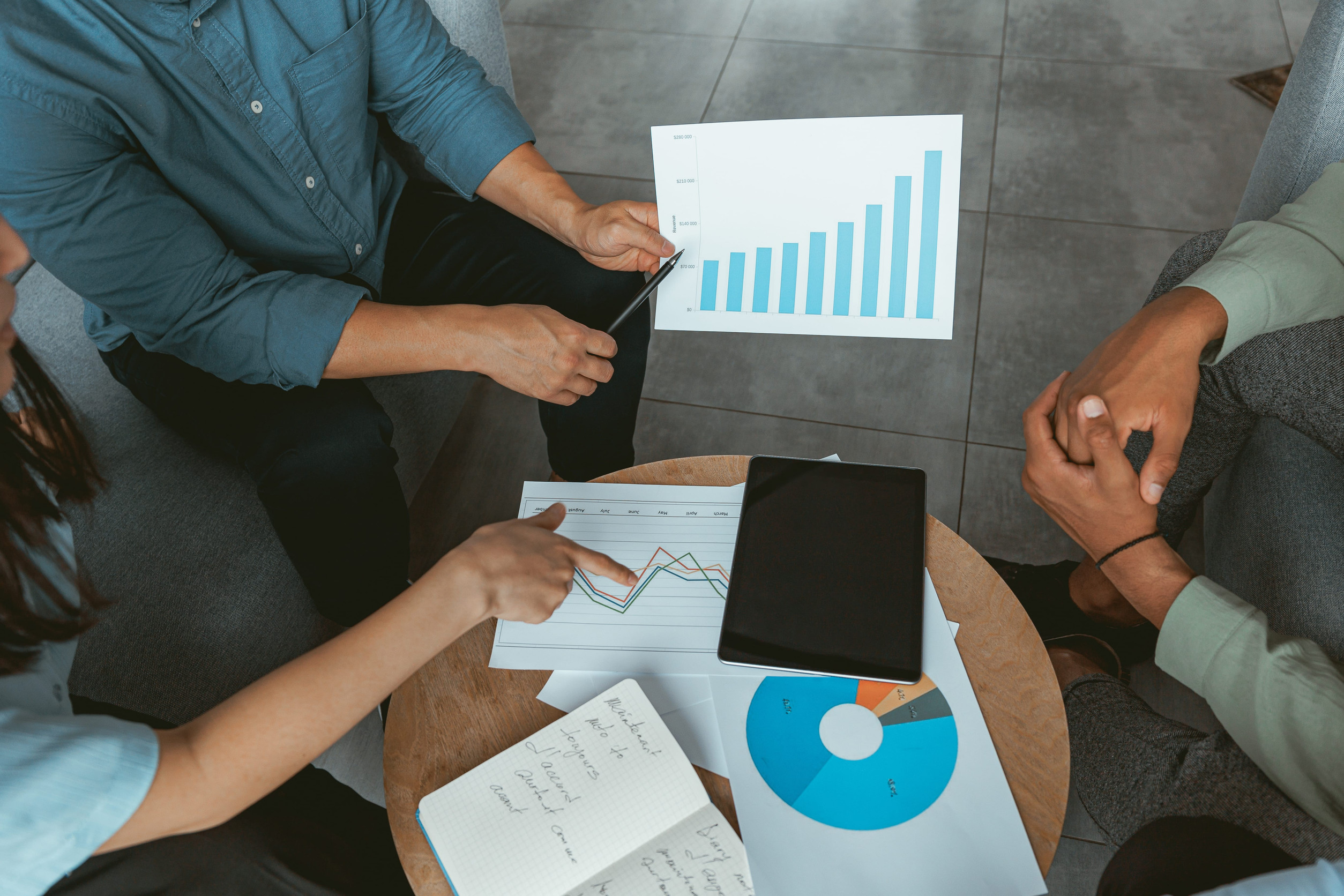 Three professionals sit around a table reviewing marketing reports, charts, and growth graphs during a strategy meeting, discussing campaign performance and business lead generation.