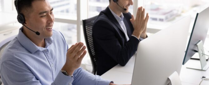 Two sales representatives wearing headsets work at desktop computers in a bright office, demonstrating customer communication, teamwork, and sales conversations that help convert leads into customers.