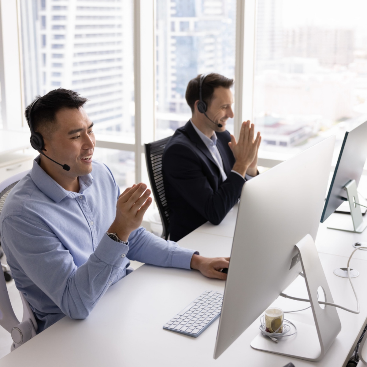 wfasdf9234 Two sales representatives wearing headsets work at desktop computers in a bright office, demonstrating customer communication, teamwork, and sales conversations that help convert leads into customers.